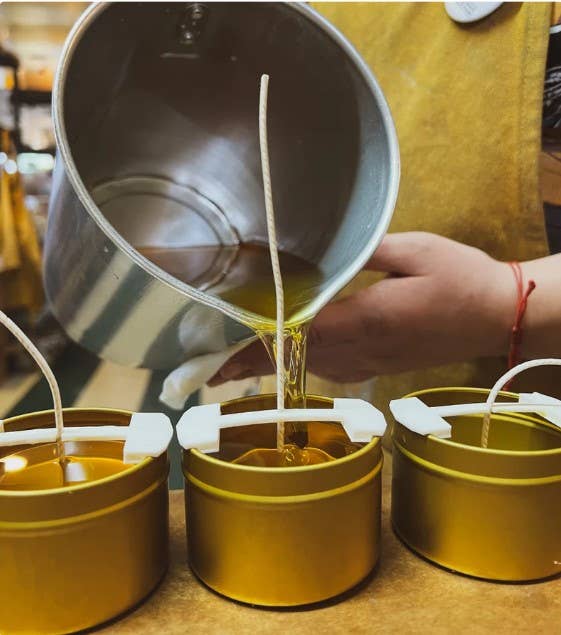 Person pouring liquid into small metal containers on a wooden surface.